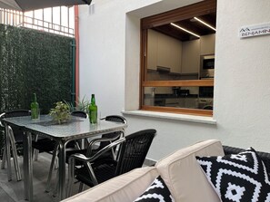 A patio with a table, chairs, a sofa, and a window overlooking a kitchen.