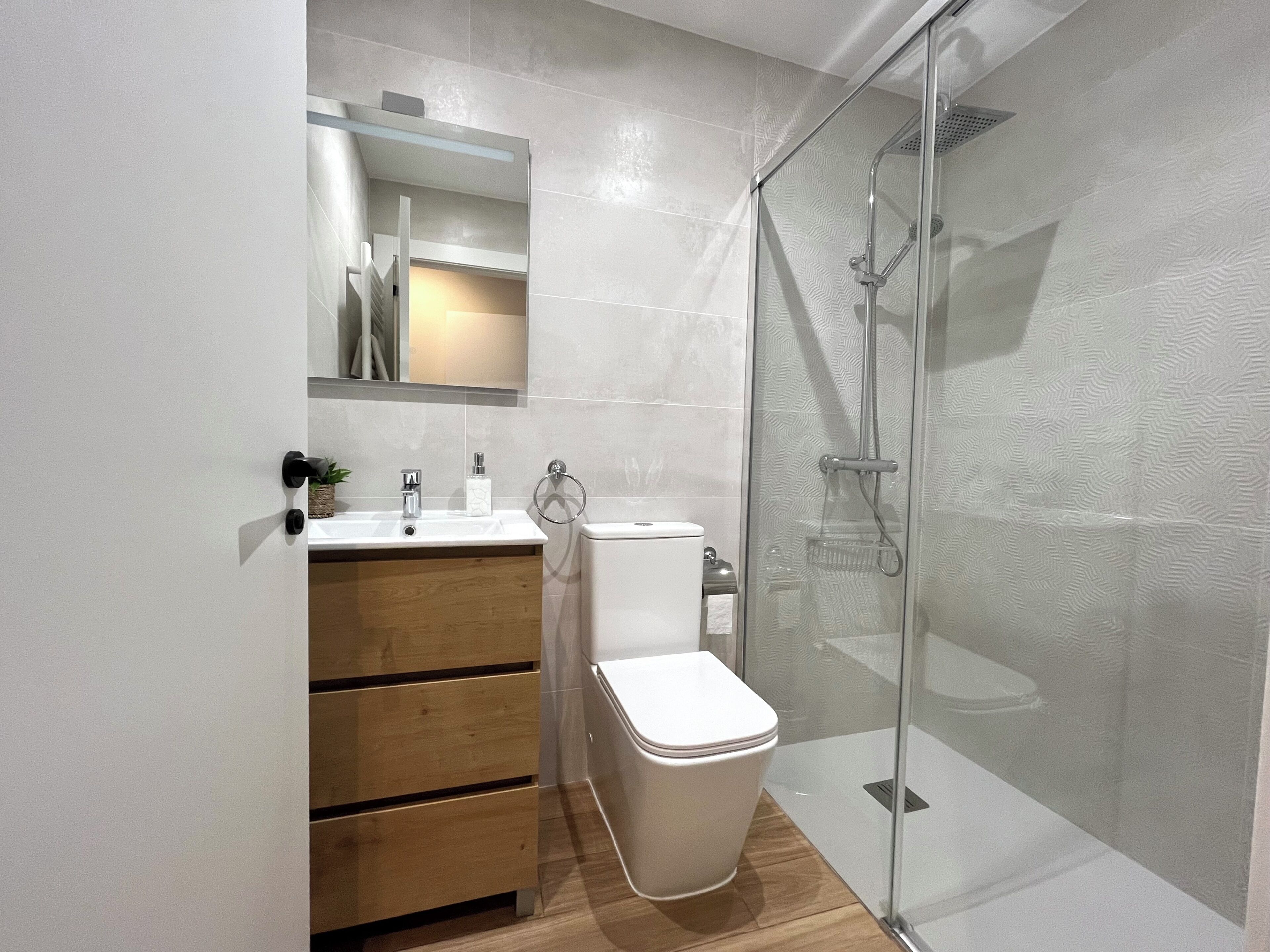 Une salle de bain moderne avec une douche à parois de verre, un meuble-lavabo en bois et des toilettes blanches.