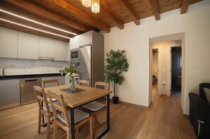A modern kitchen with wooden beams, a dining table with chairs, a refrigerator, and a potted plant.