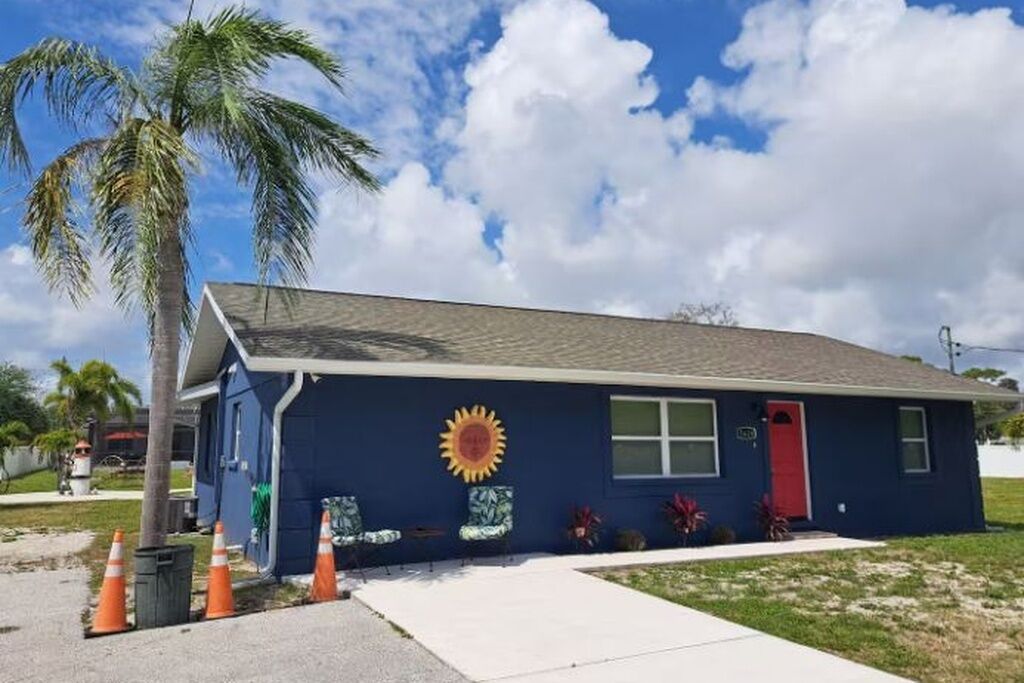 A single-story building with a red door, a blue exterior, and a sun mural.