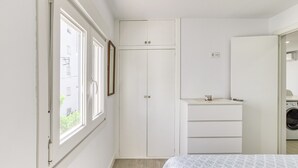 Una camera da letto con un letto, un armadio, un bagno piccolo con lavatrice e una finestra vista edifici.
