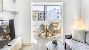 Un soggiorno moderno con una TV a schermo piatto, un tavolo da pranzo in vetro con sedie, un divano e una lampada.