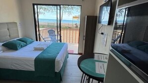 Een kamer met een bed, een bureau, een stoel en uitzicht op het strand.