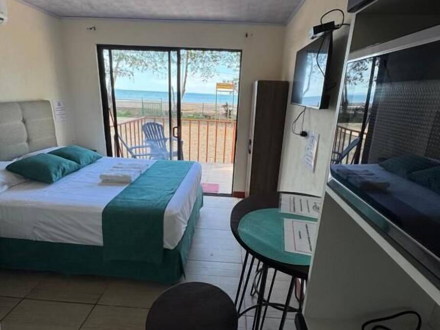 A room with a bed, a desk, a chair, and a view of the beach.