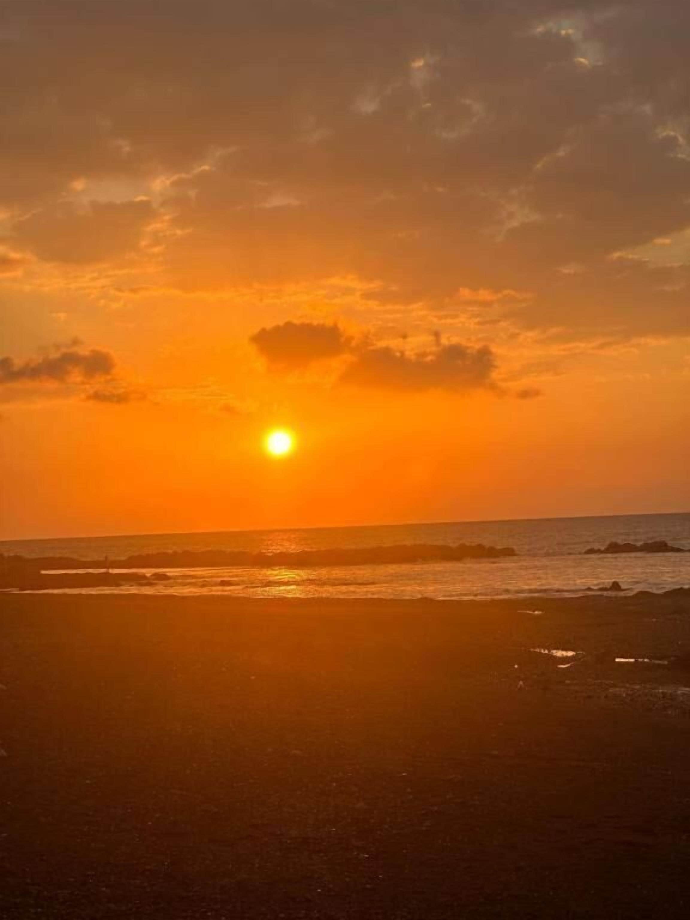 A sunset over a beach with waves and a clear sky.