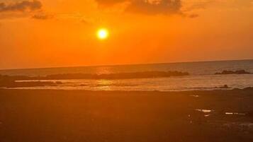 A sunset over a beach with waves and a clear sky.