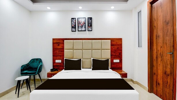A bedroom with a large bed, a wooden headboard, a nightstand, a chair, and a door. - Collection O Hotel Evergreen (Faridabad)