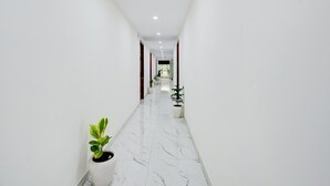 A corridor with white walls, marble flooring, and potted plants. - Collection O Hotel Evergreen (Faridabad)