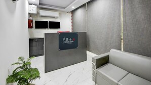 A reception area with a grey couch, a reception desk with a 'Collection' sign, a plant, and a TV on the wall. - Collection O Hotel Evergreen (Faridabad)