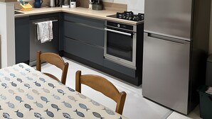 Eine moderne Küche mit integriertem Mikrowellenherd, Backofen und Kühlschrank, einem Esstisch mit Stühlen und einer Tischdecke mit Muster.