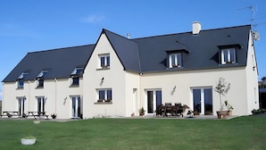 Ein großes, zweistöckiges Gebäude mit Flachdach, zahlreichen Fenstern und einer einladenden Veranda mit Gartenmöbeln.
