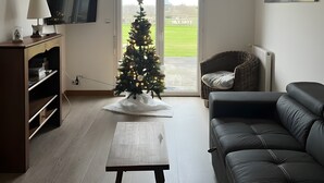 Ein Wohnzimmer mit Fernseher, Weihnachtsbaum, Sofa und einem Gemälde an der Wand.