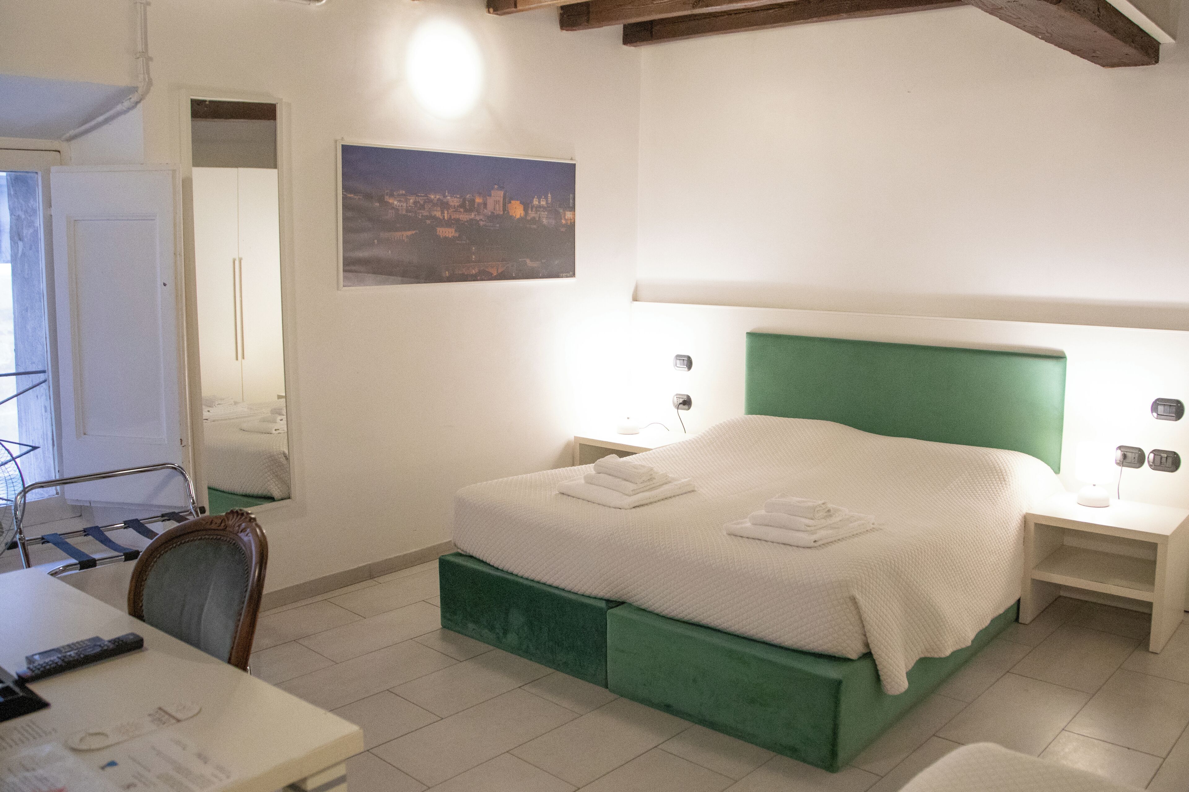 A bedroom with a bed, bedside tables, a chair, a desk, and a mirror.