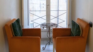 Une pièce avec deux fauteuils orange, une petite table et une vue sur un espace extérieur accessible par une porte, cet espace étant délimité par une rambarde en métal.