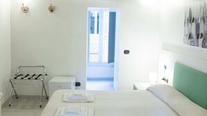 Une chambre d’hôtel comprenant un lit, un climatiseur fixé au mur, un porte-serviettes et une porte donnant sur une autre pièce.