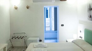 Une chambre d’hôtel comprenant un lit, une chaise, une table, un appareil de climatisation et une porte donnant sur une autre pièce.