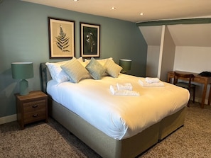 A neatly made bed with pillows, a bedside table, a lamp, and framed botanical artwork on the wall.
