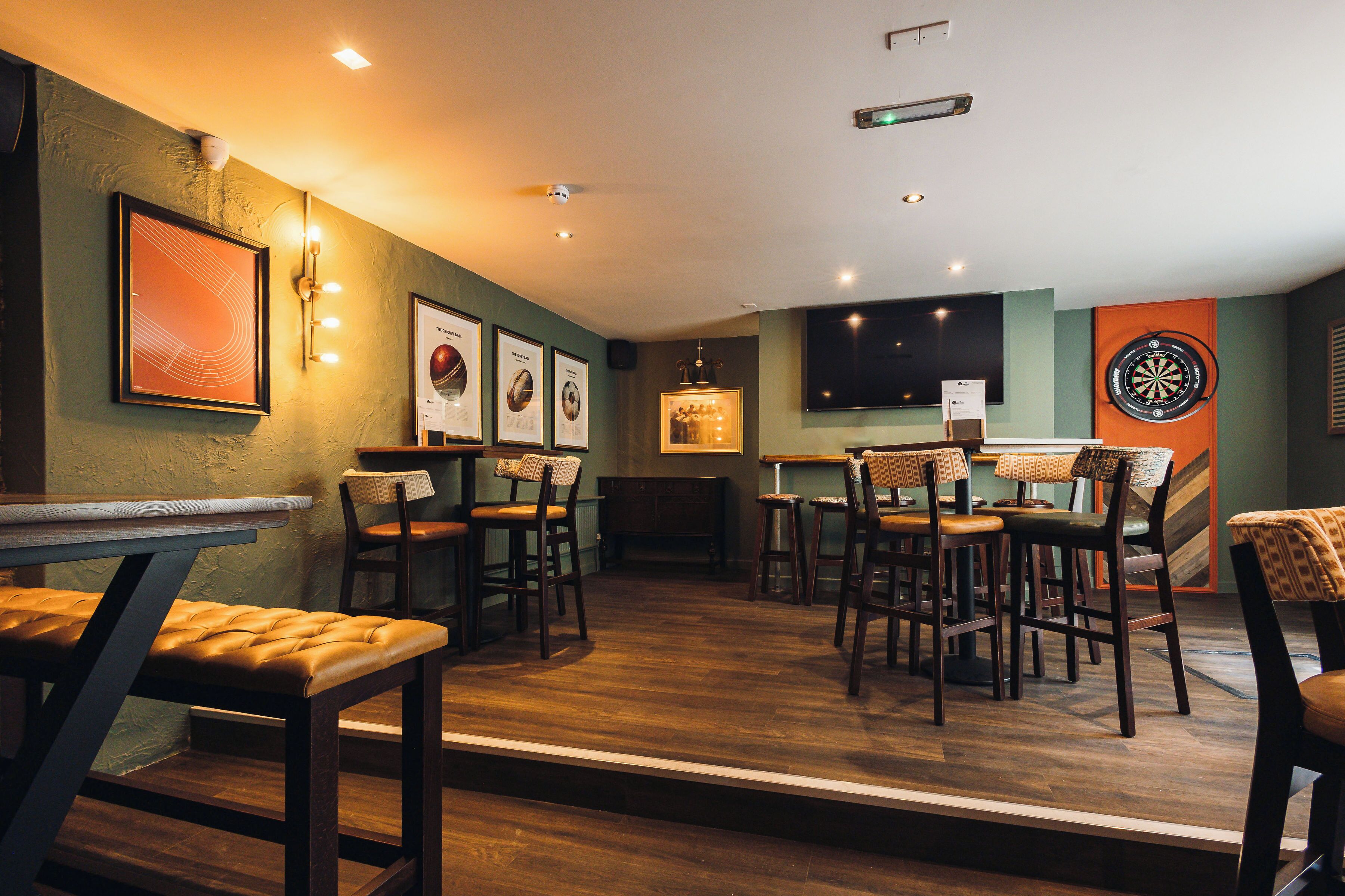 A restaurant with wooden tables and chairs, framed pictures on the wall, and a dartboard.