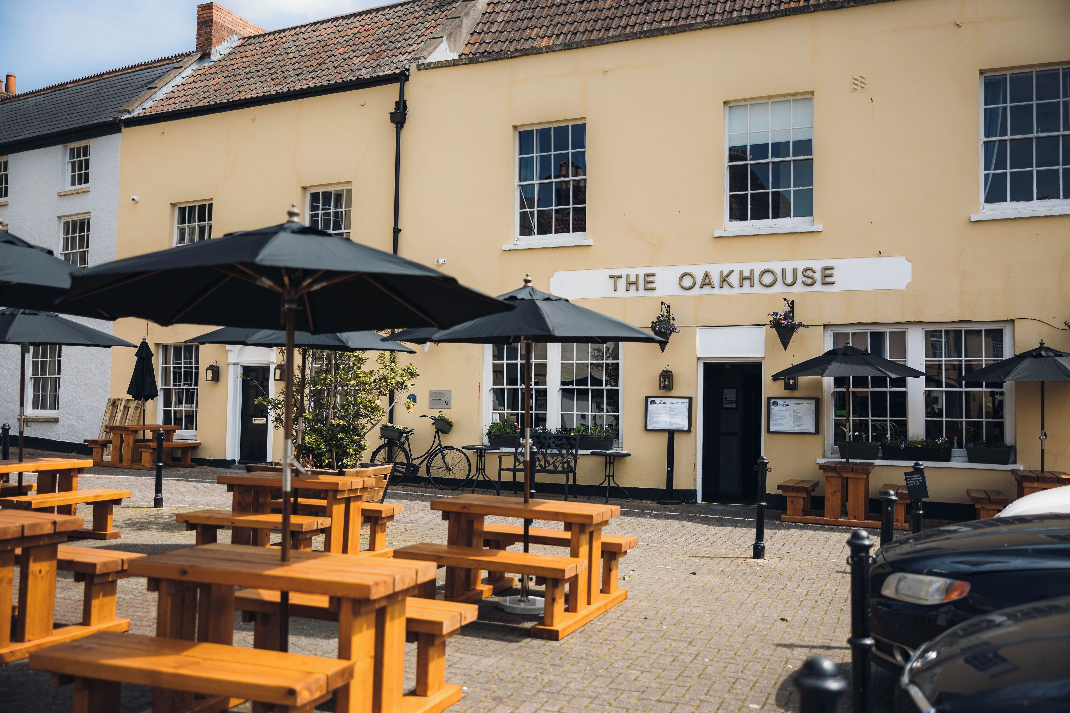 An outdoor seating area with wooden tables and black umbrellas at The Oakhouse.