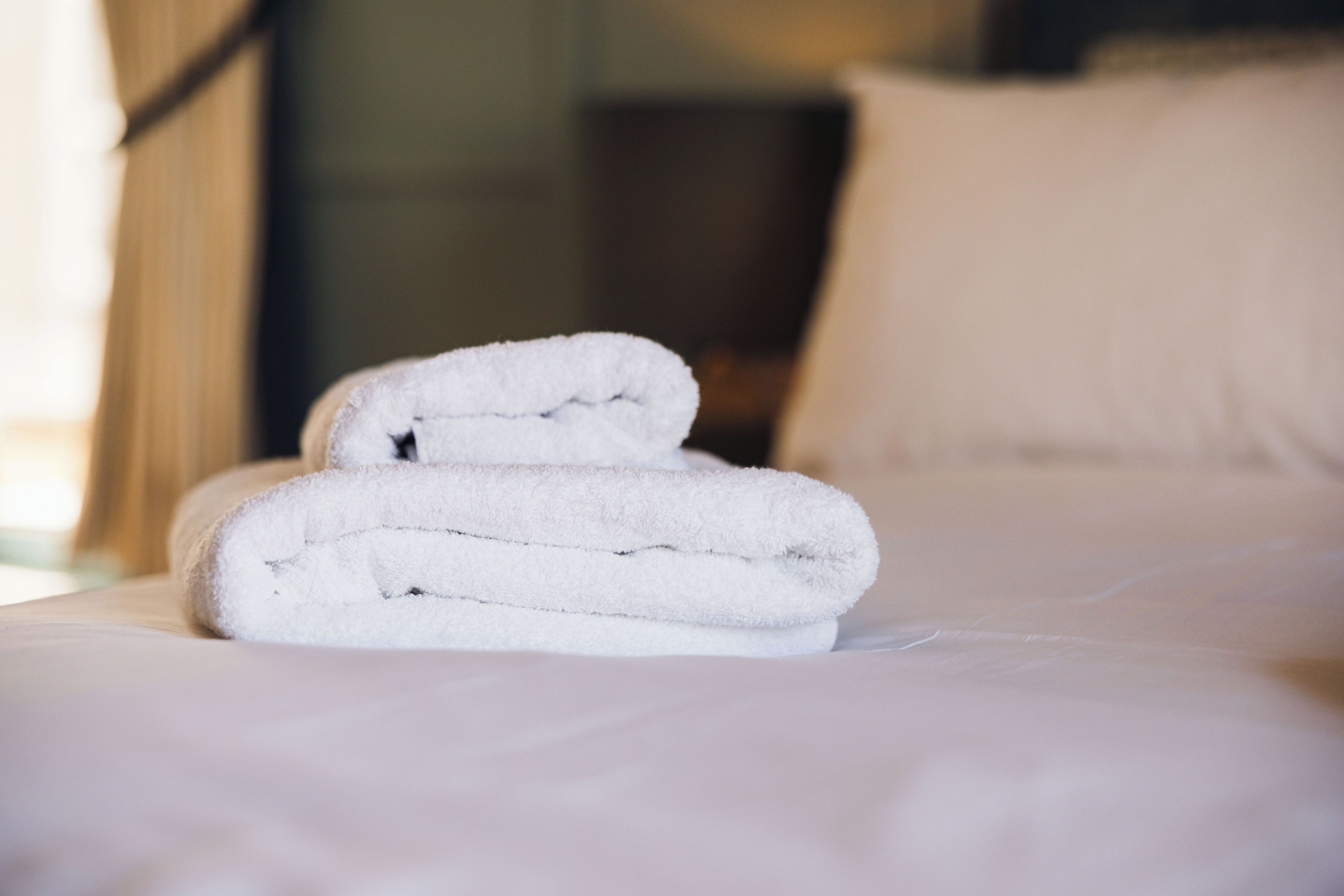 A neatly folded white towel on a bed with a white pillow.