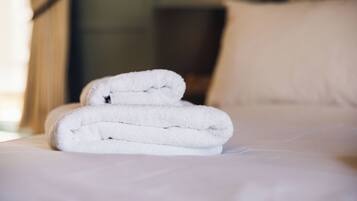 A neatly folded white towel on a bed with a white pillow.