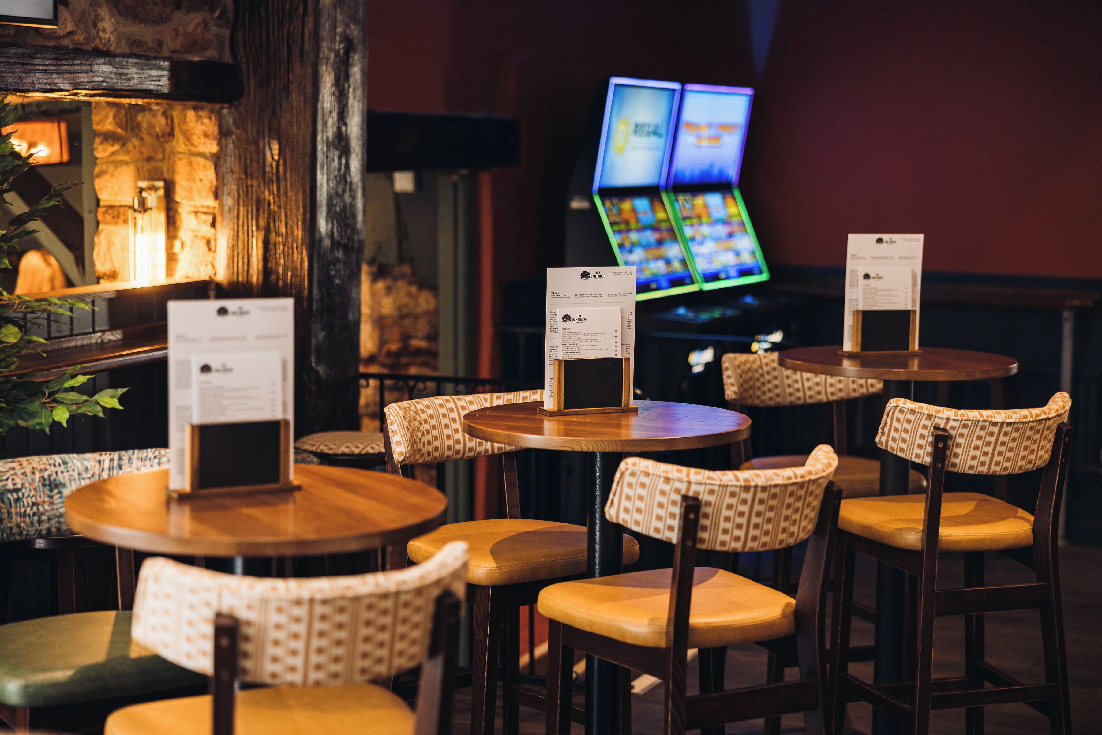 A restaurant with round tables and patterned chairs, menu boards, and a television screen in the background.