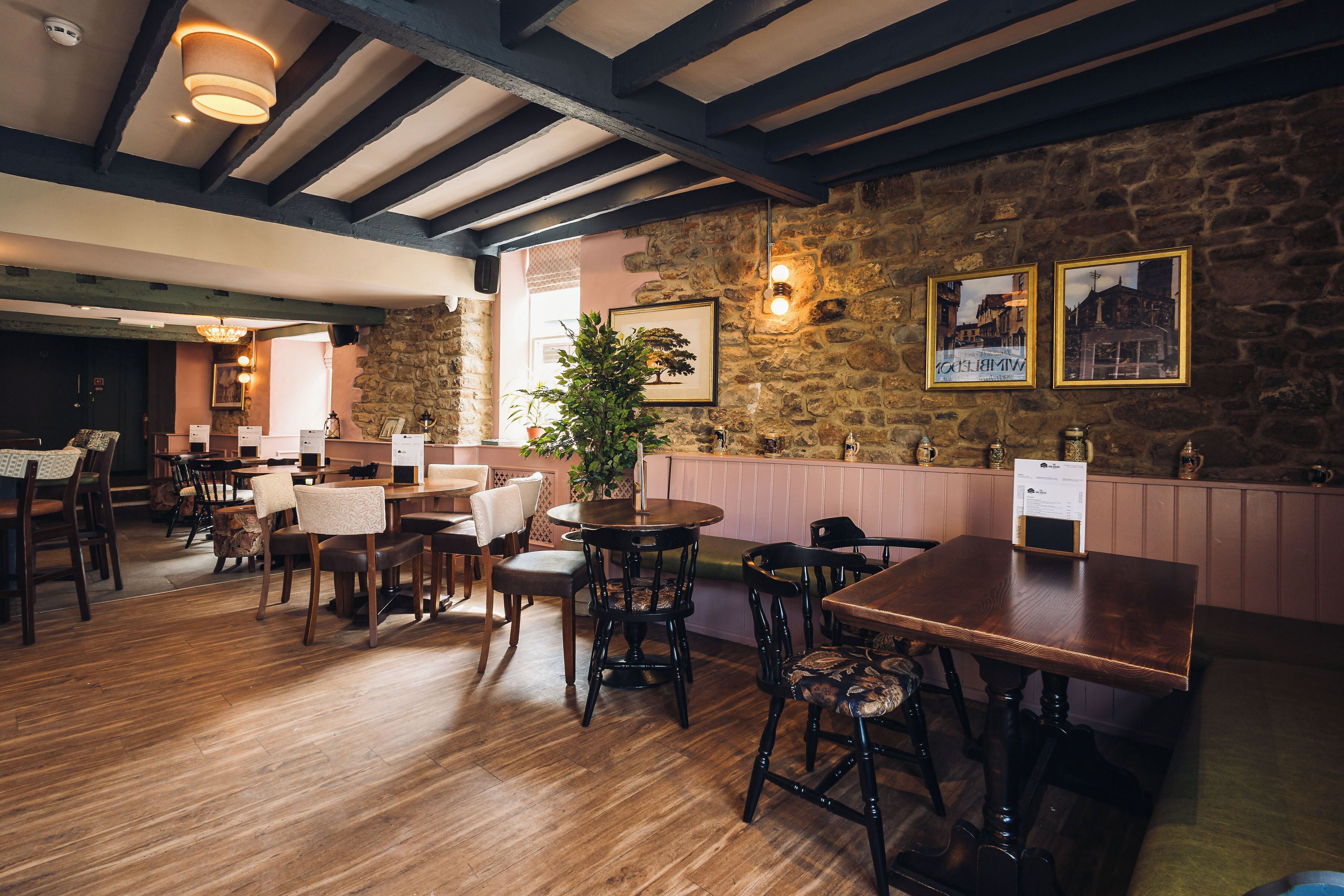 Interior de restaurante con mesas y sillas de madera, paredes de piedra y cuadros en las paredes.