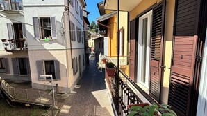 A narrow cobblestone street flanked by buildings with balconies, a metal fence, and potted plants. - House Eliana apartment Moon A stone's throw from the lake (Meina)