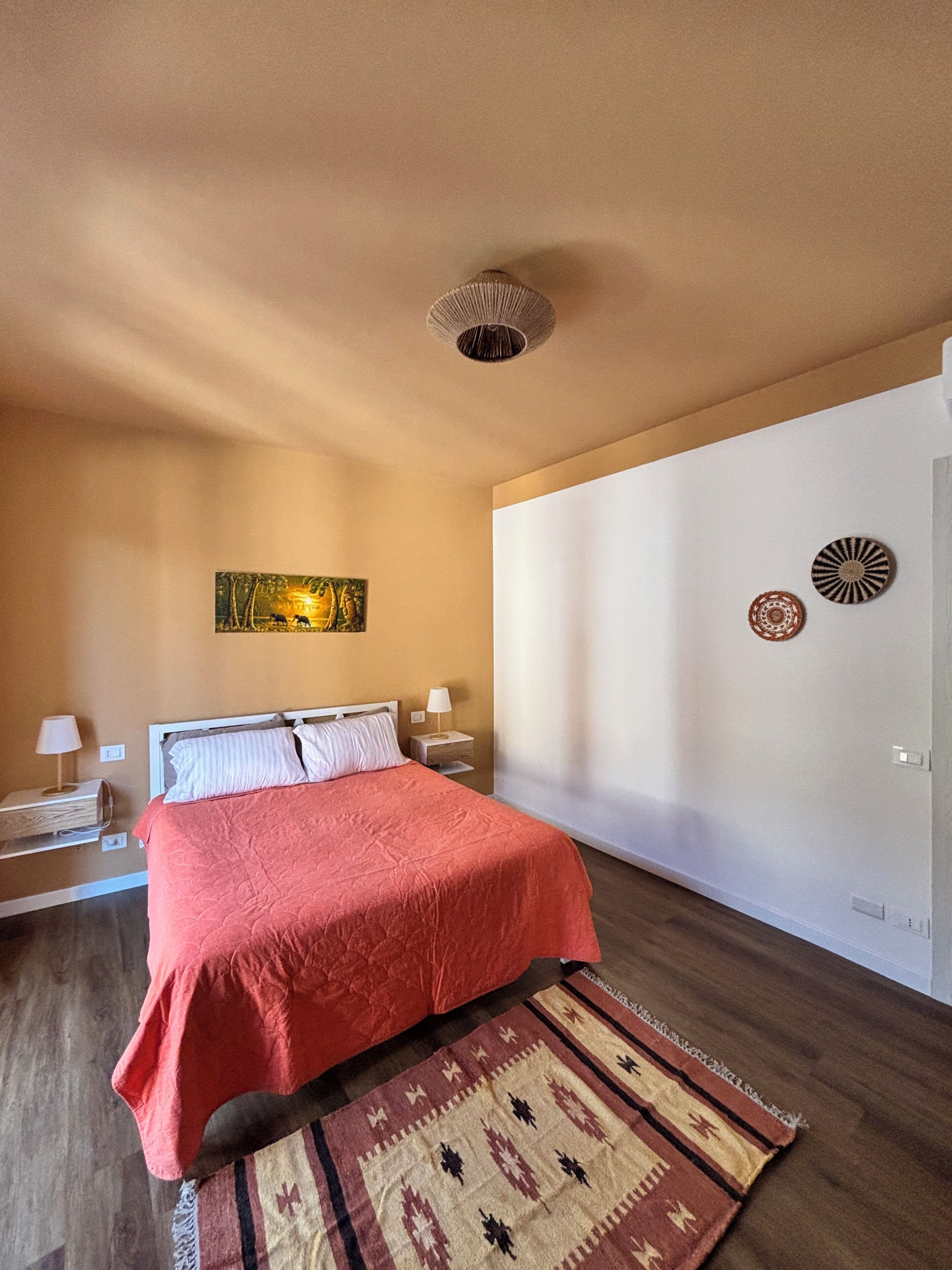A bedroom with a bed, nightstands, a wall art piece, and a patterned rug.