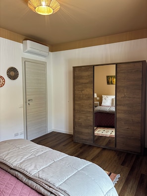 A bedroom with a bed, wardrobe, and an air conditioning unit. - House Eliana apartment Moon A stone's throw from the lake (Meina)