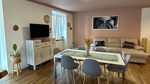 A living room with a dining table, chairs, a sofa, a TV, and a painting on the wall. - House Eliana apartment Moon A stone's throw from the lake (Meina)