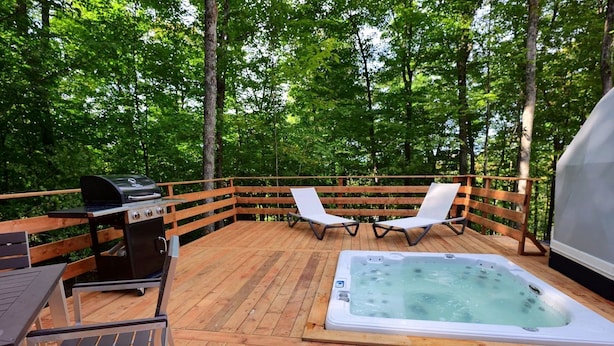 A wooden deck with a hot tub, a grill, and two lounge chairs.