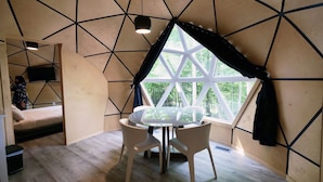 A room with a geometric ceiling design, a large window with curtains, a round table with chairs, and a bed.