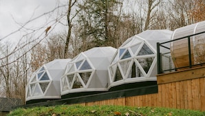 A series of geodesic dome structures with large windows, wooden walls, and a grassy foreground.