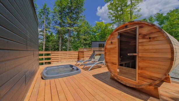 Una terraza de madera con sauna, sillas de descanso y una cabaña de madera.