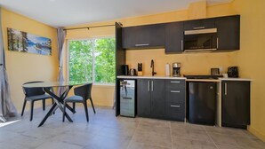 Una cocina compacta con comedor, una ventana con vistas a la vegetación y un cuadro en la pared.