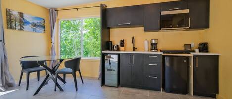 Una cocina compacta con comedor, una ventana con vistas a la vegetación y un cuadro en la pared.