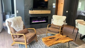 A modern living room with a fireplace, two leather armchairs, a coffee table, and a television mounted on the wall. - Bel Air Tremblant L'ETOILE : 2 CHAMBRES, JACUZZI PRIVÉ (La Conception)
