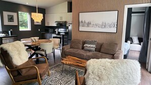A modern living room with a sofa, chairs, a coffee table, and a dining area. - Bel Air Tremblant L'ETOILE : 2 CHAMBRES, JACUZZI PRIVÉ (La Conception)