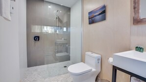 A modern bathroom with a glass-enclosed shower, a toilet, and a sink with toiletries.