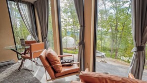 A room with large windows, a glass table, leather chairs, and a view of a road and trees.