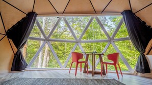 Una habitación con un ventanal grande, dos sillas rojas, una mesita y una cortina negra.