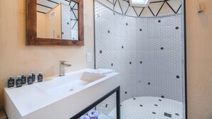 Un baño con lavamanos blanco, espejo y ducha con diseño hexagonal.