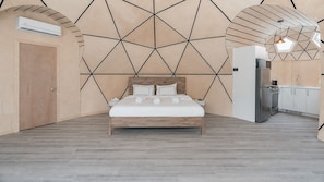 A modern bedroom with a geometric wall design, a wooden bed, and a kitchenette area. - Bel Air Tremblant MICKEY DÔME : 1 LIT KING, JACUZZI ET SAUNA (La Conception)