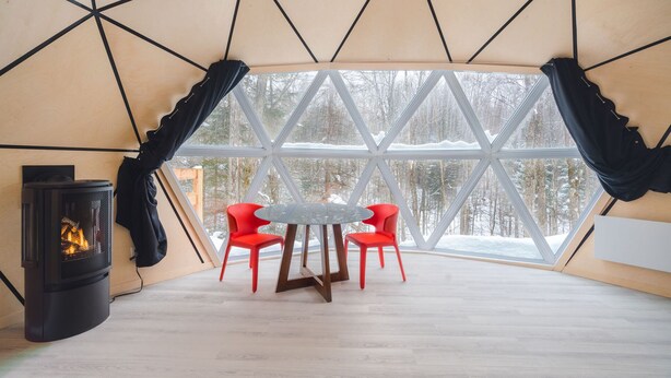 Una habitación acogedora con una estufa de leña, una mesa redonda y dos sillas rojas.