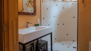 Un baño con lavamanos blanco, espejo y ducha con diseño geométrico en el techo.
