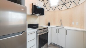 Una cocina compacta con un refrigerador de acero inoxidable, una estufa negra y una encimera blanca.