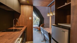 A compact kitchen with a built-in stove, a refrigerator, and a dining area with a chair. - Bel Air Tremblant DÔME MEZZANINE : 1 KING, 2 SIMPLE, JACUZZI, SAUNA-450PI (La Conception)