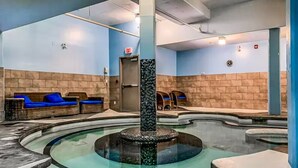 Een wellnessruimte met een centraal gelegen whirlpool, zitgedeeltes en een deur met de aanduiding 'EXIT'.