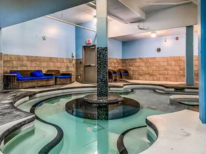 A spa area with a central hot tub, seating areas, and a door marked 'EXIT'. - Lovely 2BR Rockies Getaway w Pool + Hot Tub Access (Canmore)